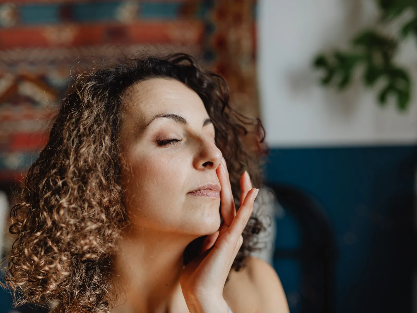 A woman with curly hair resting her fingertips on her cheek with her eyes closed