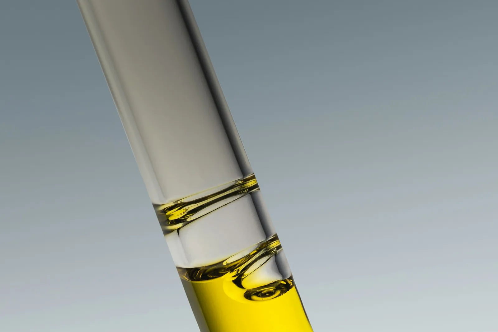 A glass pipette holding a drop of golden serum