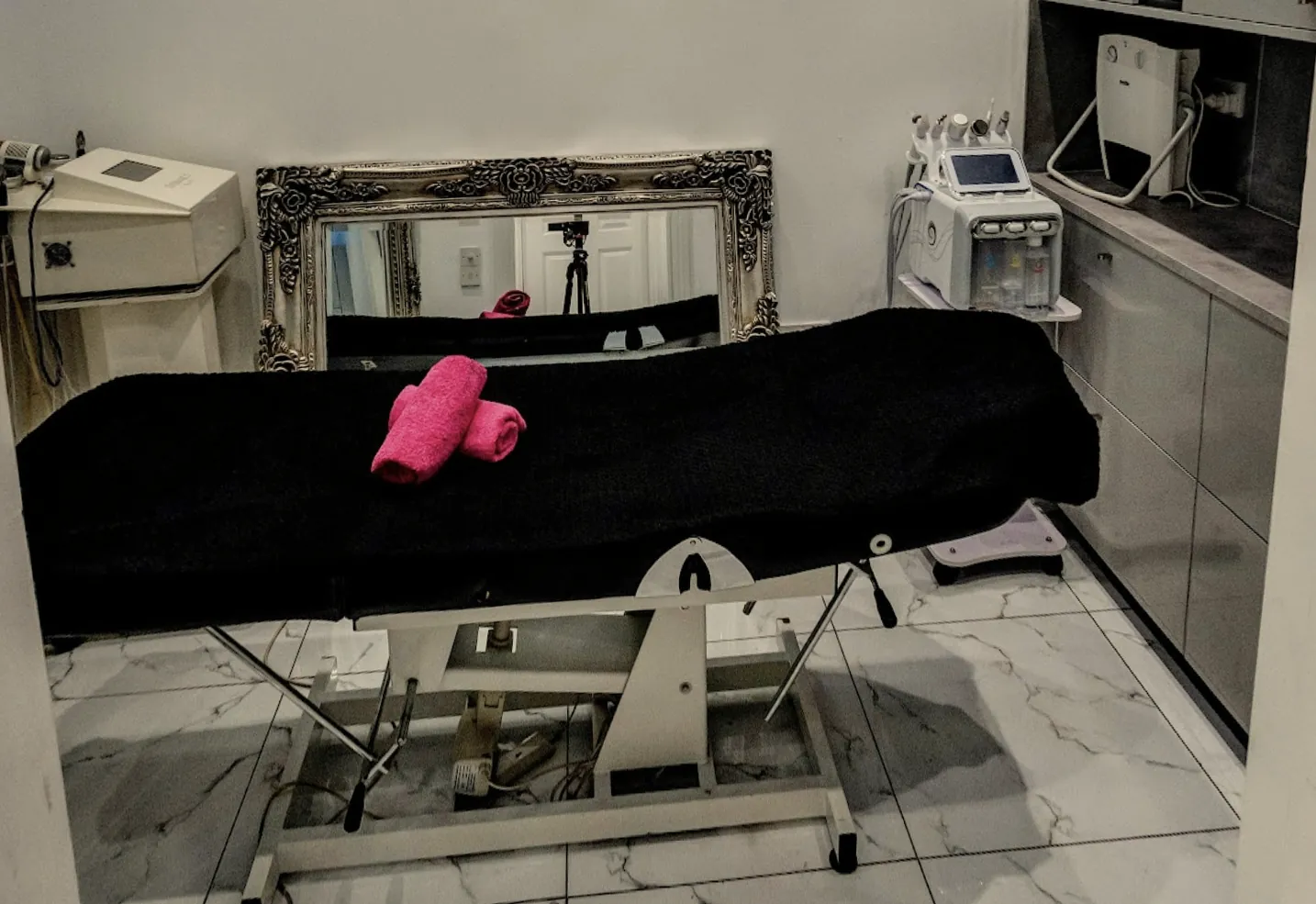 A private treatment room with a facial couch laid with towels and a hydro-facial machine