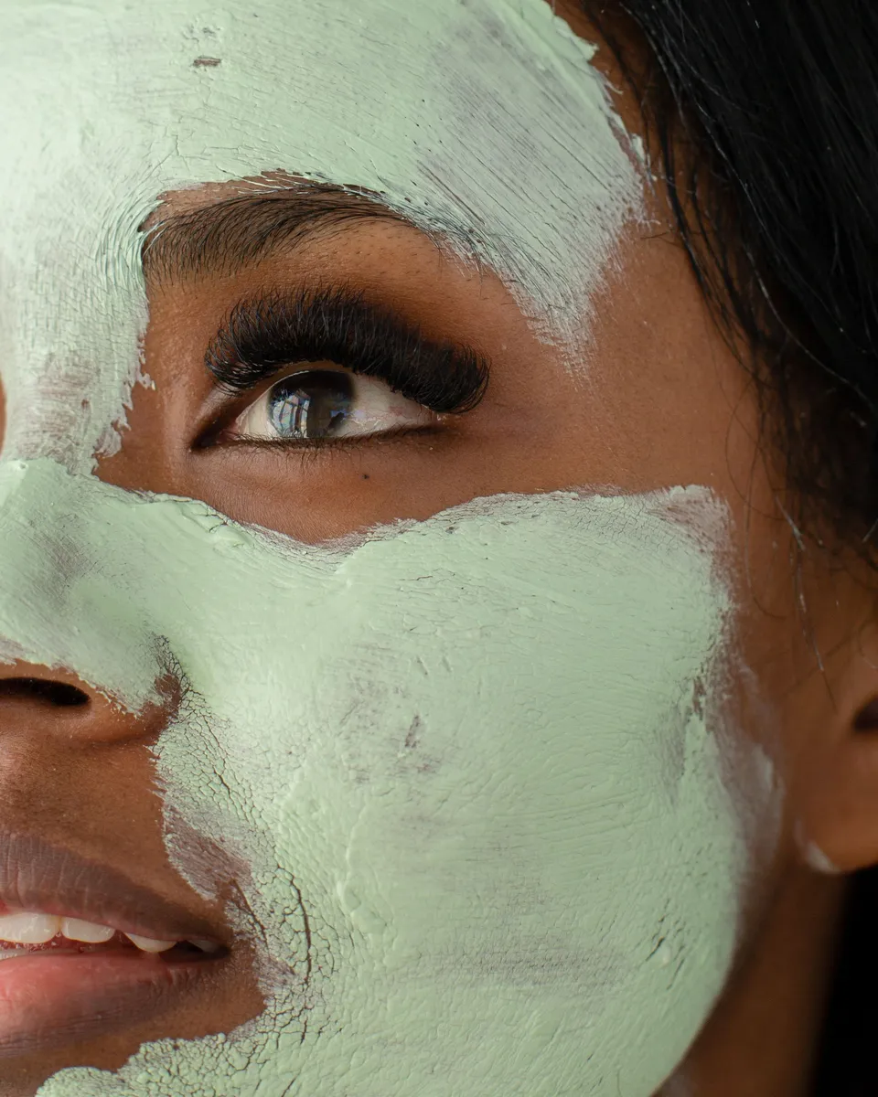 A smiling woman wearing a green clay face mask