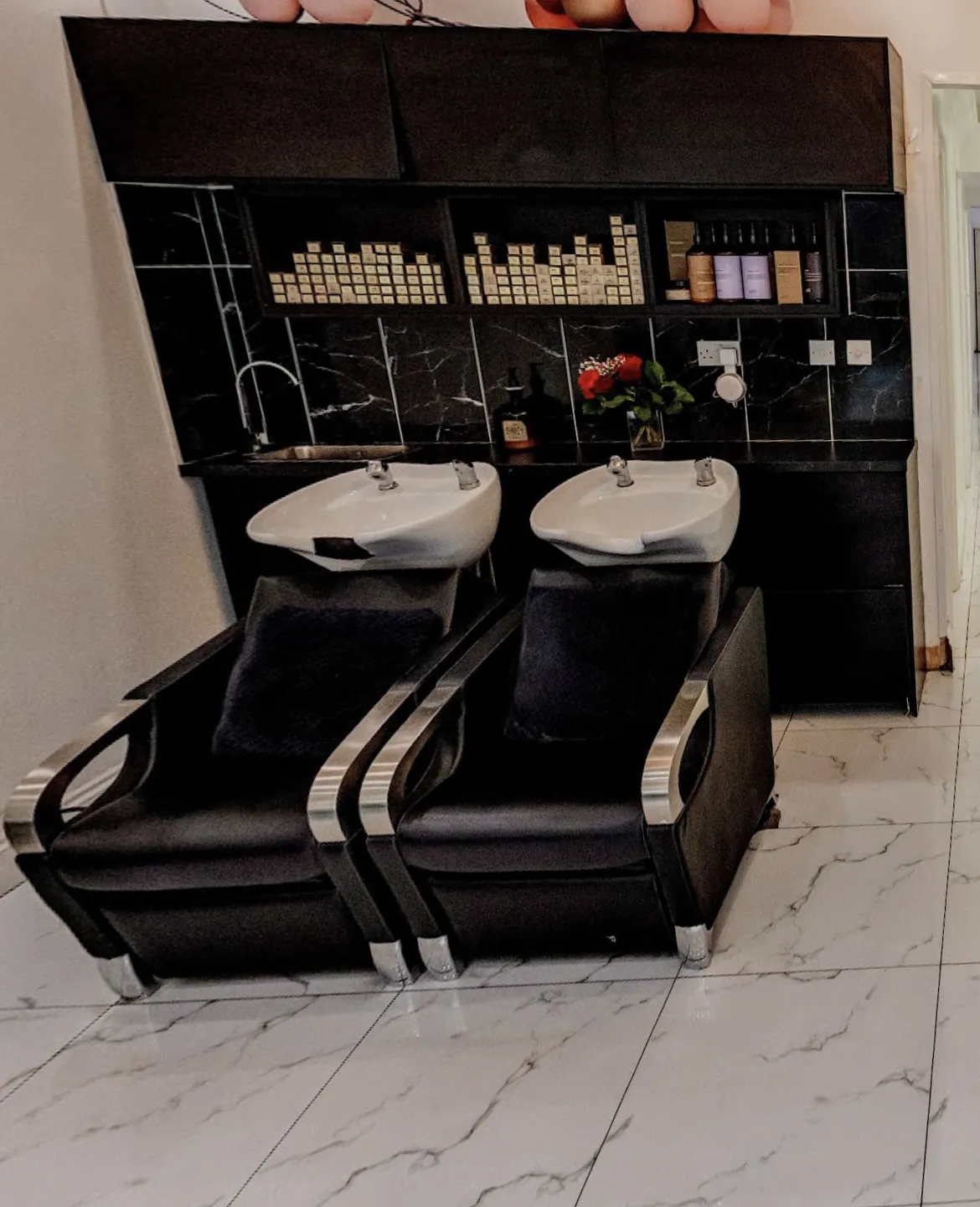 Two backwash basins and chairs in front of a black marble wall