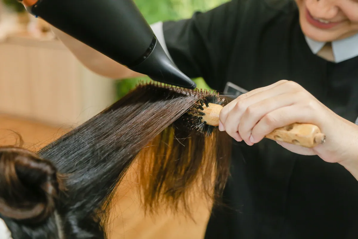 A stylist blow drying long dark hair over a round brush