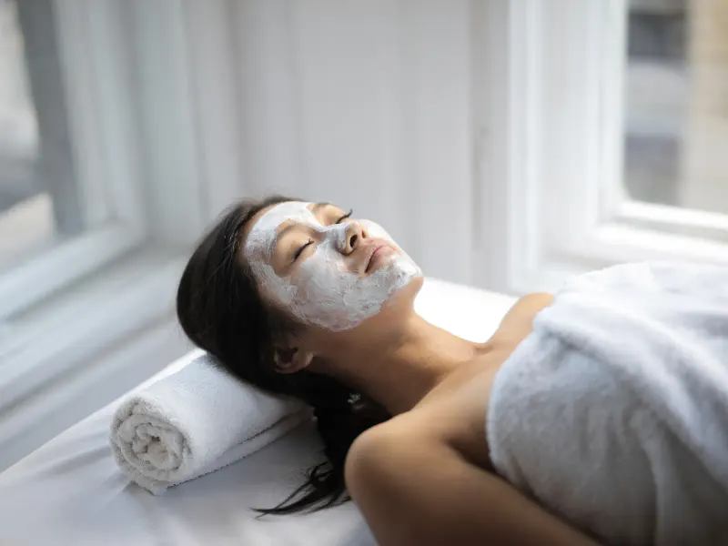 A woman with a cream face mask lying on a couch with her eyes closed