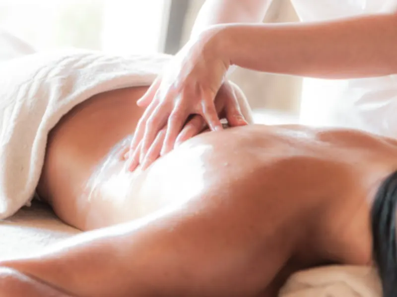 A therapist's hands massaging a client's back on a couch