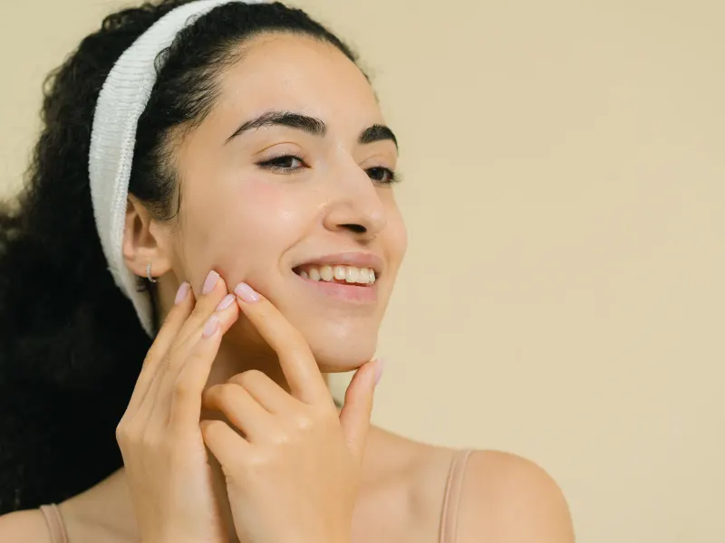 A smiling woman in a white headband touching her cheek