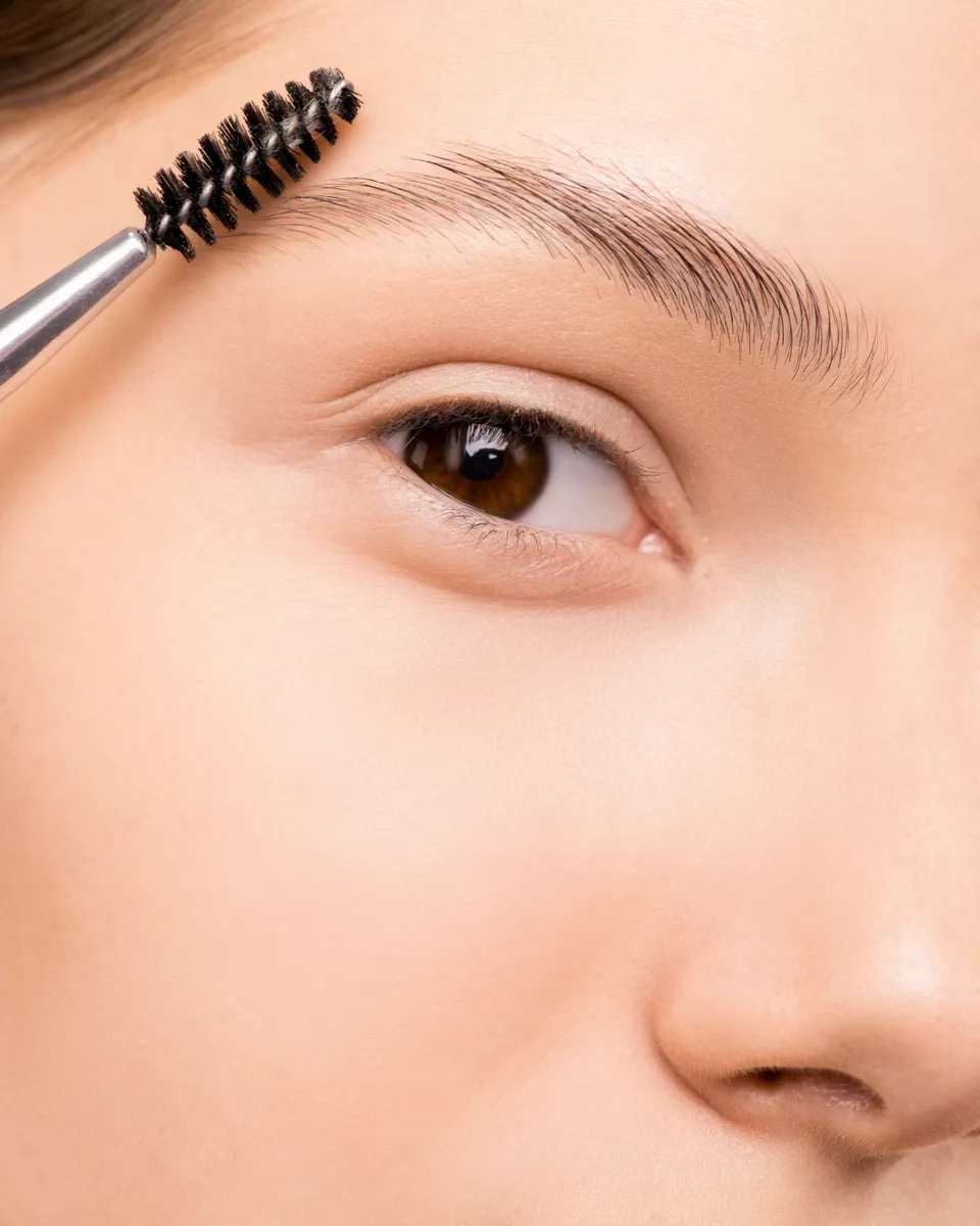 A spoolie brush combing a woman's eyebrow upwards