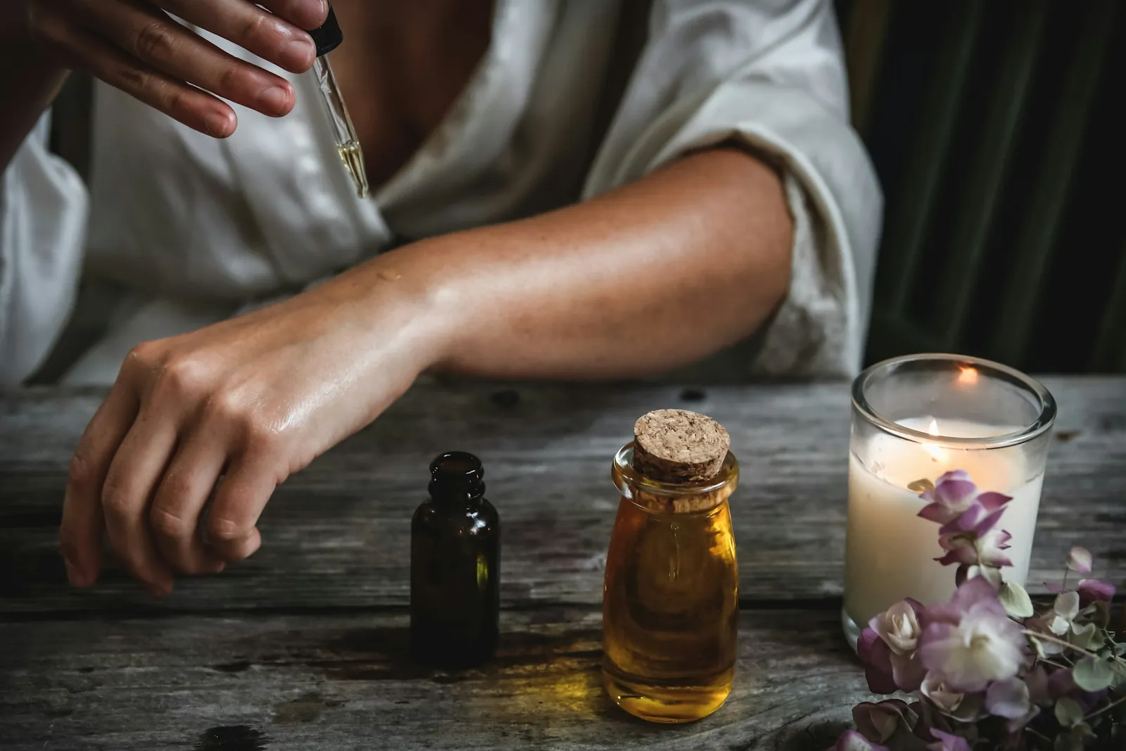Massage oils in glass bottles beside a lit candle and dried flowers
