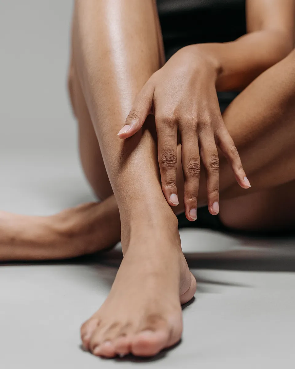 A woman sitting on a grey floor with her legs crossed and one hand resting on her shin