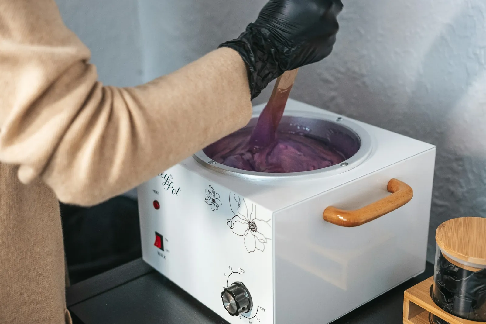 A gloved hand stirring warm wax in a wax heater